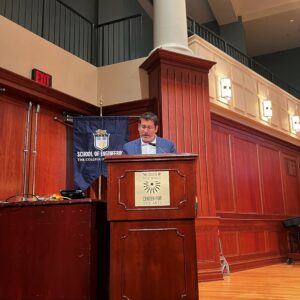 A photo of a man behind a podium reading off the names of those awarded.